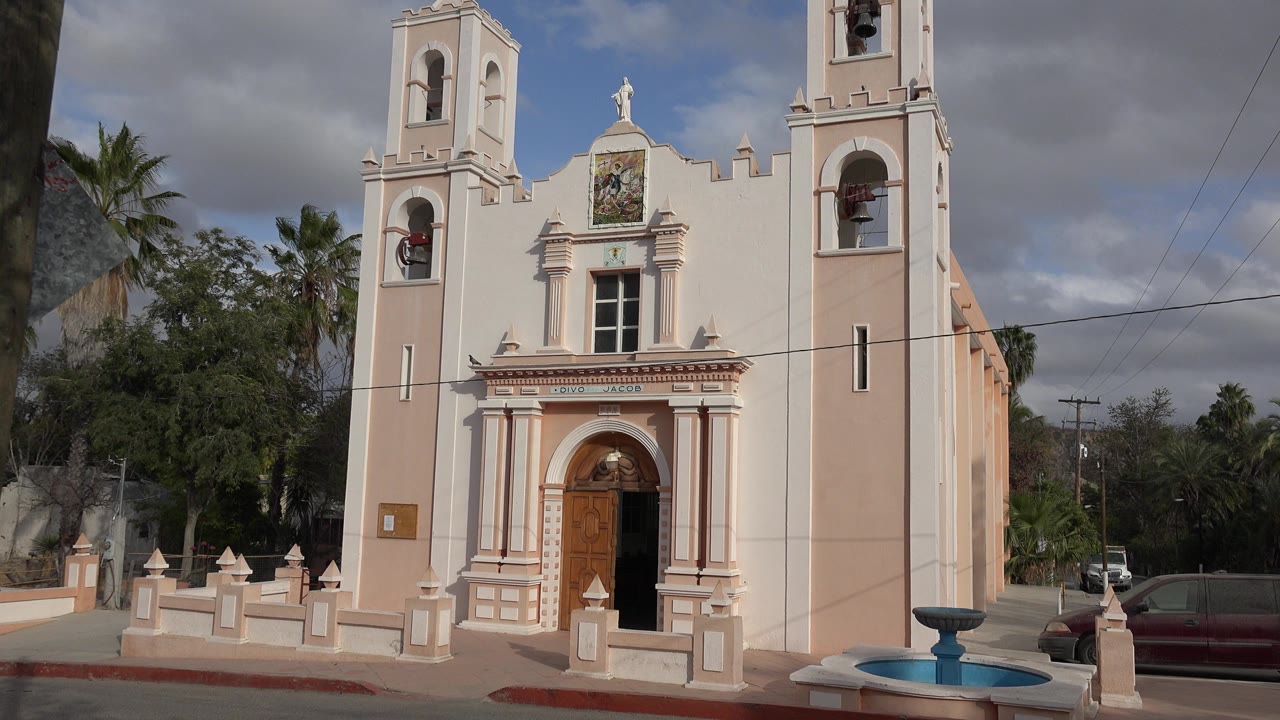 Tan and cream church facade with bell towers and a small fountain in front.