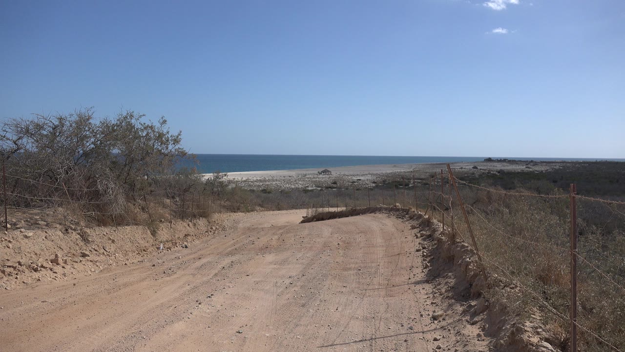 Sandy dirt road descending toward a beach and blue sea