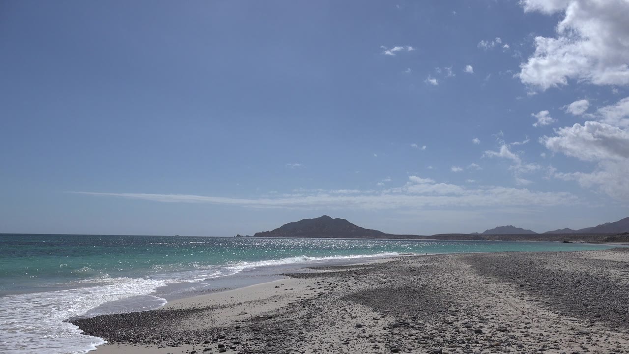 One second in, a band of white foam spreads farther across the Cabo Pulmo shoreline while the dark hill remains centered on the horizon, with no visible people.