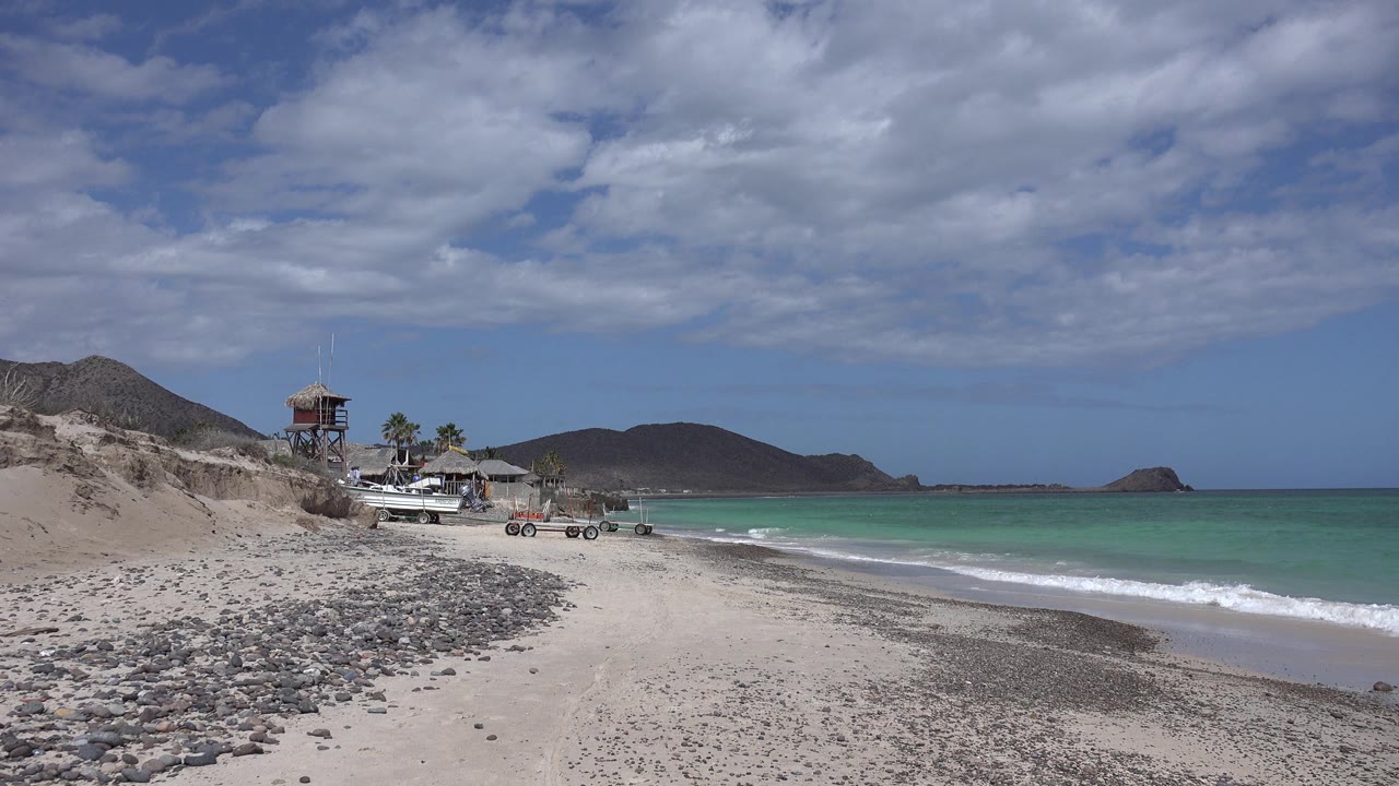 Shoreline with beach structure, palms, boats, and distant rocky islet.