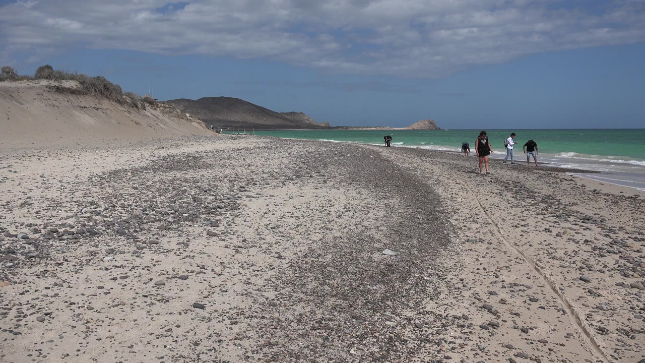 Wide beach with walkers near the surf and mountains beyond.