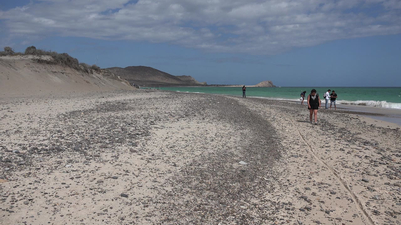 Wide beach with walkers near the surf and low hills beyond.