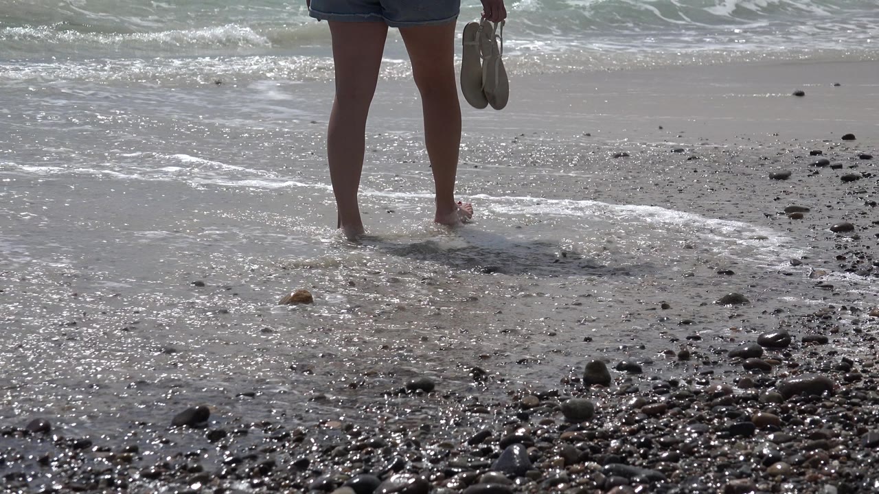 Barefoot person near receding surf and a patch of beach stones.