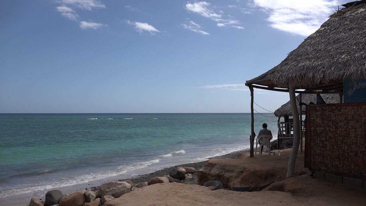 Beachfront with turquoise water, rocks, and a thatched structure at right.