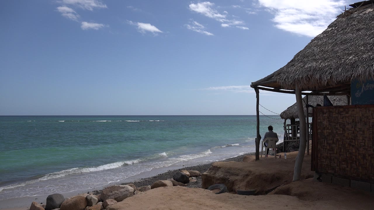 Wide beach view with turquoise water and a thatched shelter at right.