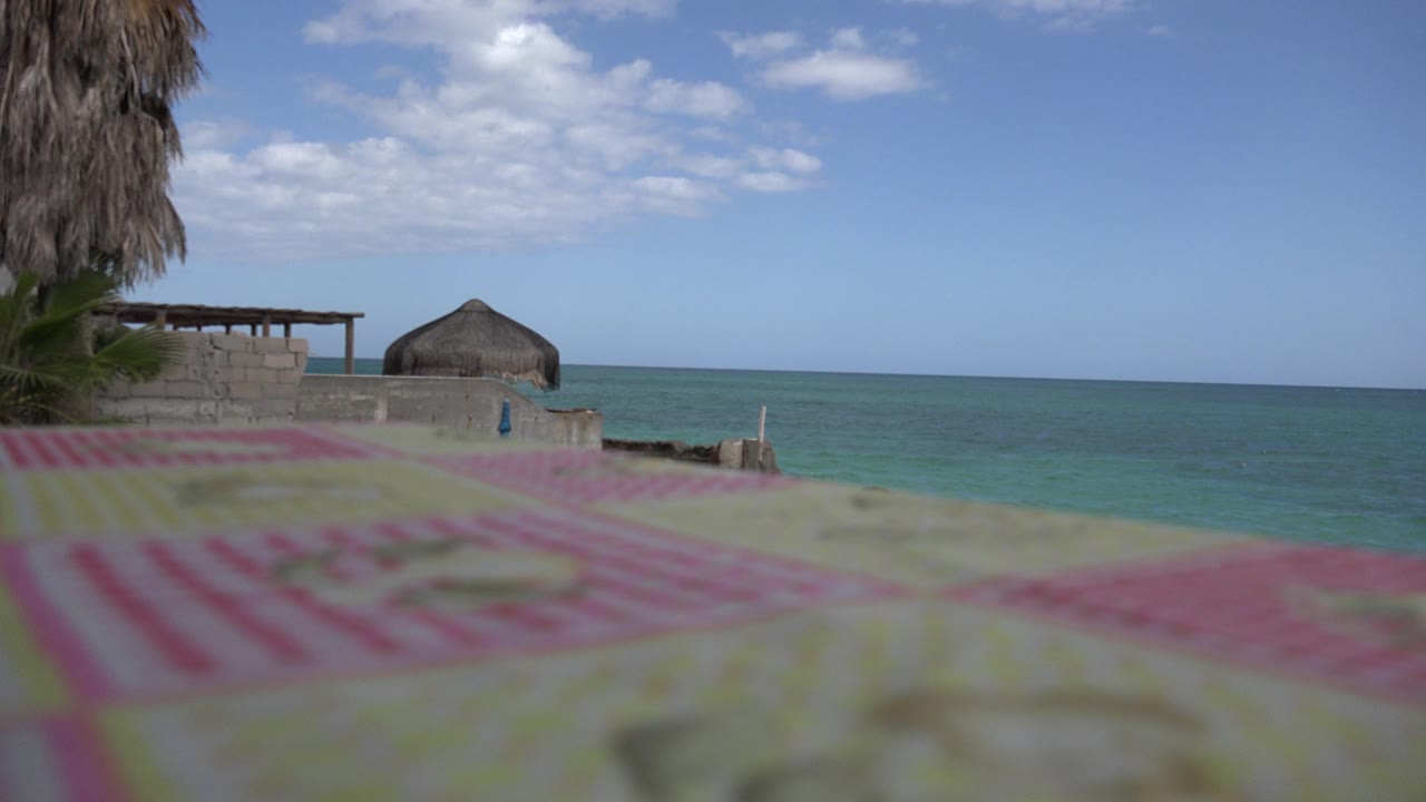 Blurred deck foreground with ocean, low wall, palm thatch, and clouds beyond.