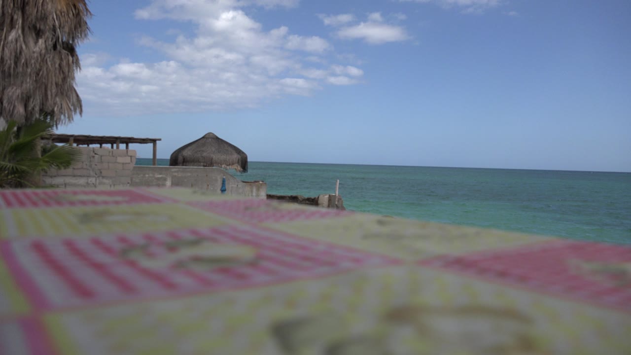 Cabo Pulmo, Mexico frame with the blurred deck surface still dominant, a low masonry wall at left, a small rounded roof near center, and the ocean line under broken clouds.