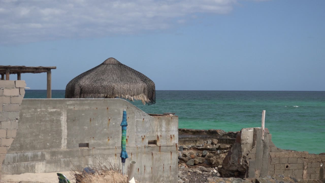 Thatched roof over rough coastal wall with green-blue sea behind.