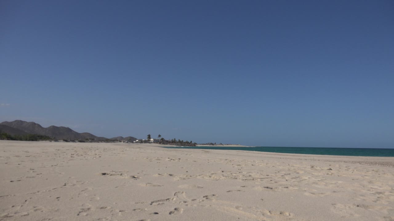 Bright beach view with empty sand, mountains, and calm sea