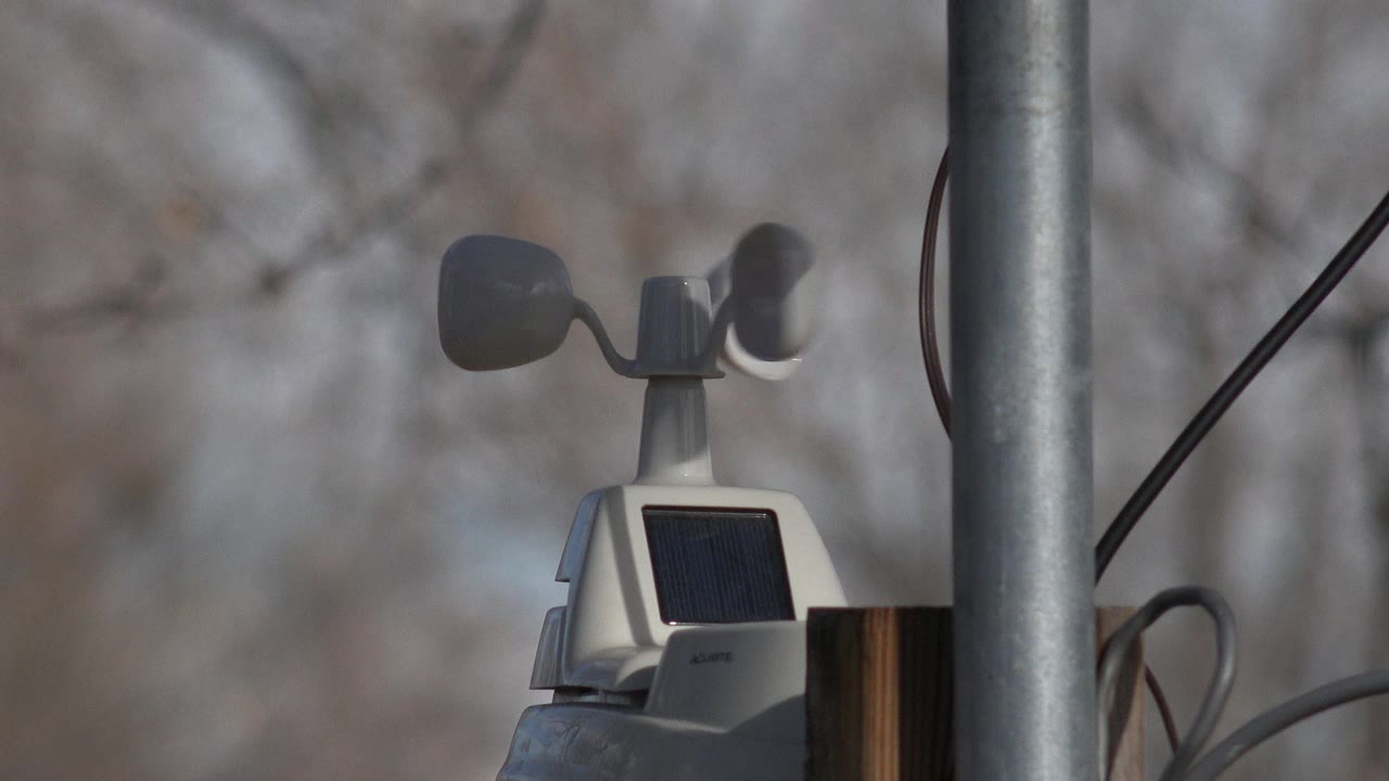 A wind speed meter with cups and a small solar panel is framed beside a vertical metal pole in Westminster, Colorado, with no visible people.