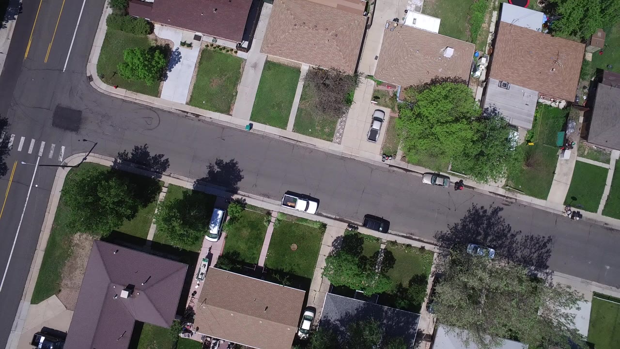 Overhead view of residential streets, rooftops, lawns, trees, and parked cars.
