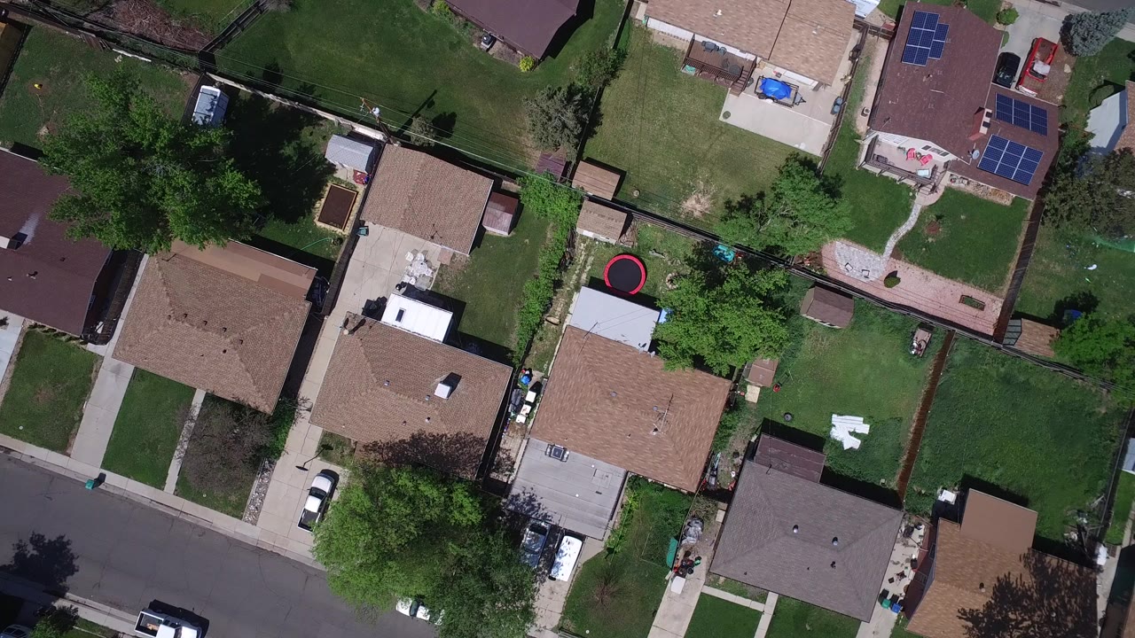 Overhead view of suburban homes, lawns, trees, and a residential street.