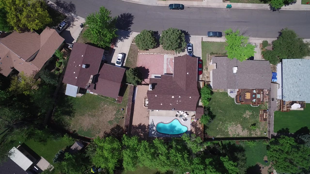 Top-down aerial view of suburban houses, a street, yards, trees, and a backyard pool.