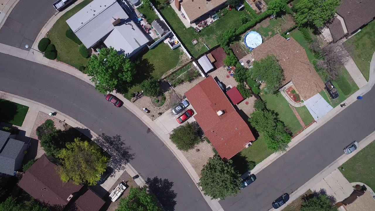 Overhead suburban street with homes, trees, driveways, and parked cars.