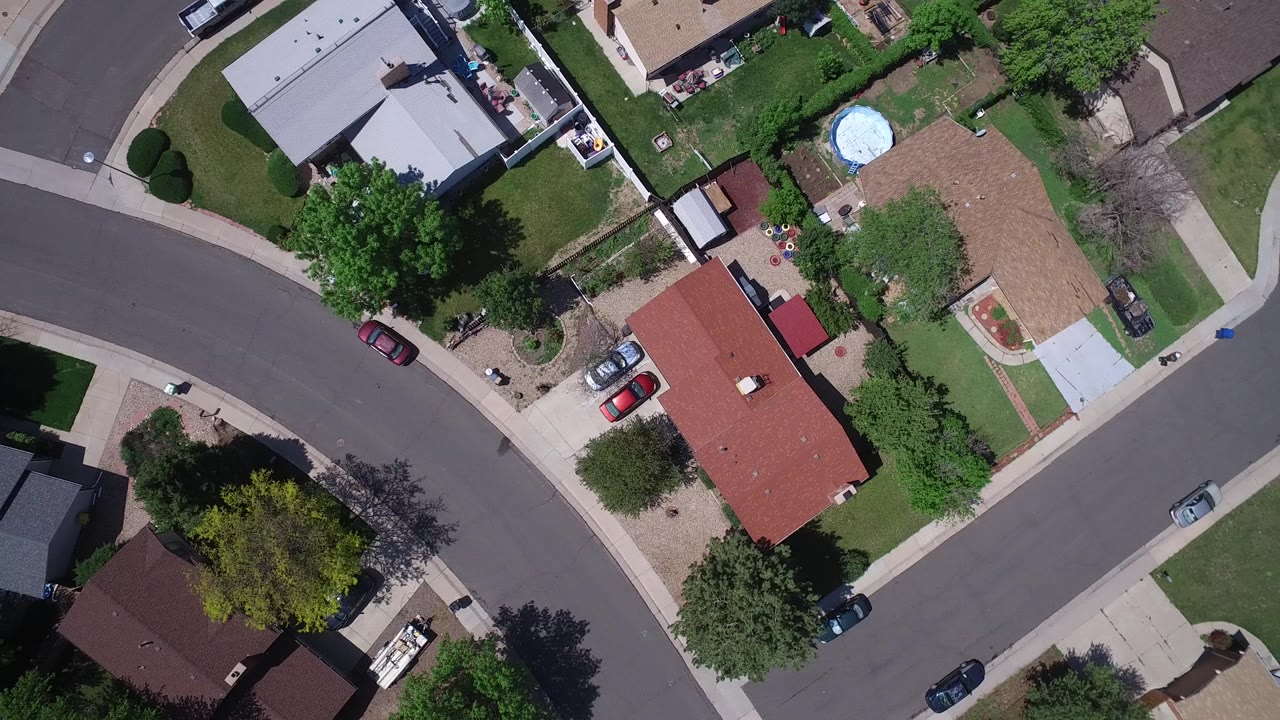 Top-down Westminster, Colorado view with a red-roof house, a tan-roof house, green lawns, sidewalks, parked vehicles, and no visible people.