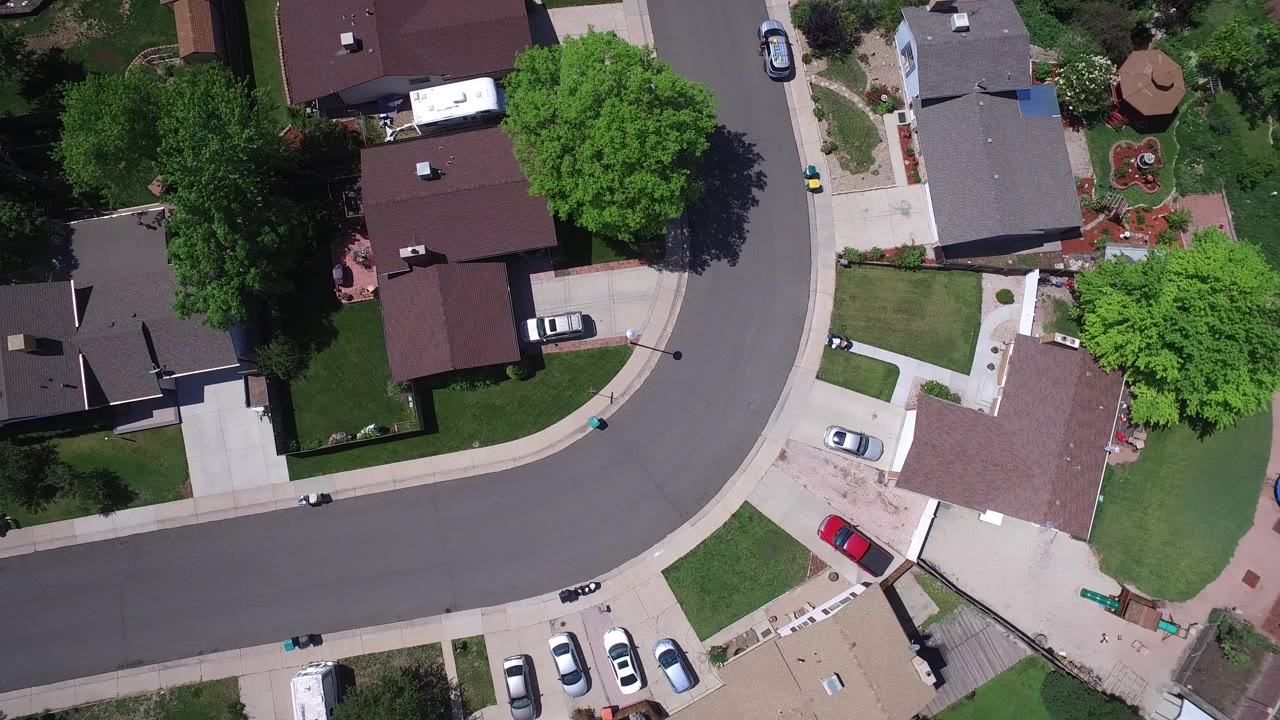 Aerial view over a Westminster, Colorado subdivision with a curved street, detached homes, green lawns, trees, driveways, and no visible people.