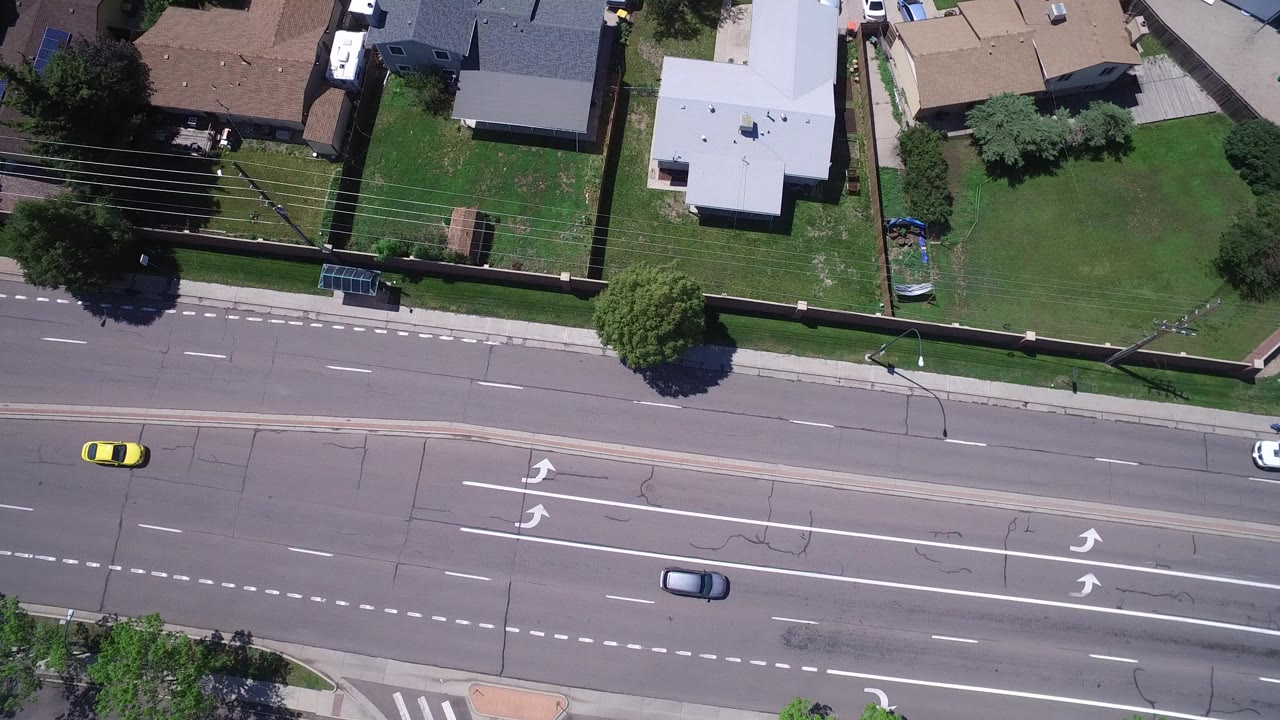 Overhead view of a multi-lane suburban road beside homes and lawns.