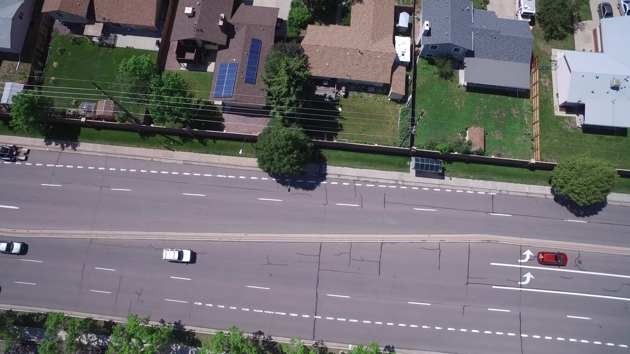 A Westminster, Colorado aerial frame shows cars spaced across several lanes, dashed white lines, turn arrows, sidewalks, and residential roofs with no visible people.