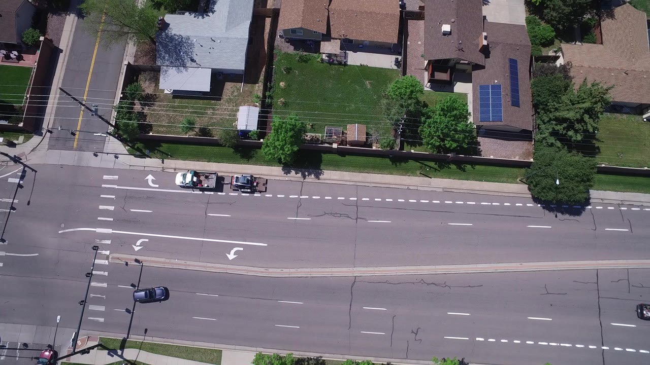 Overhead view of a multi-lane road beside homes and lawns.