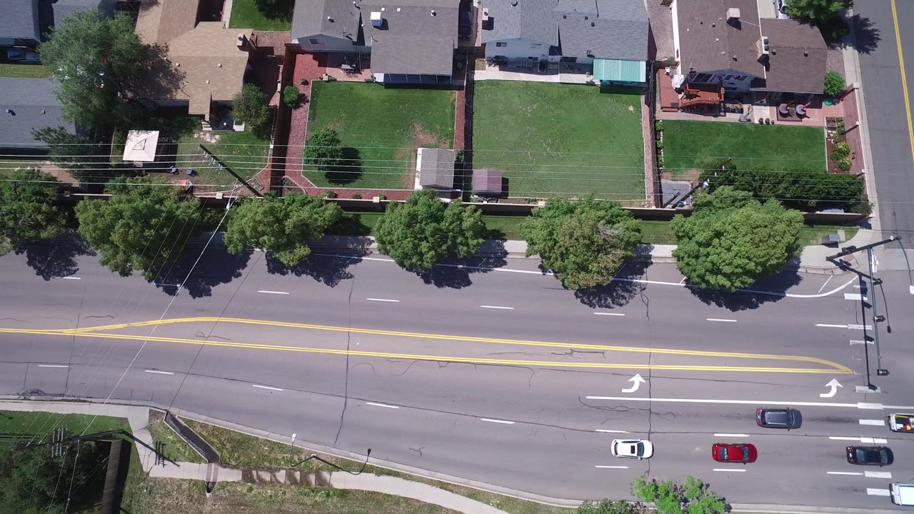 Residential rooftops and lawns above a sunlit multi-lane road.
