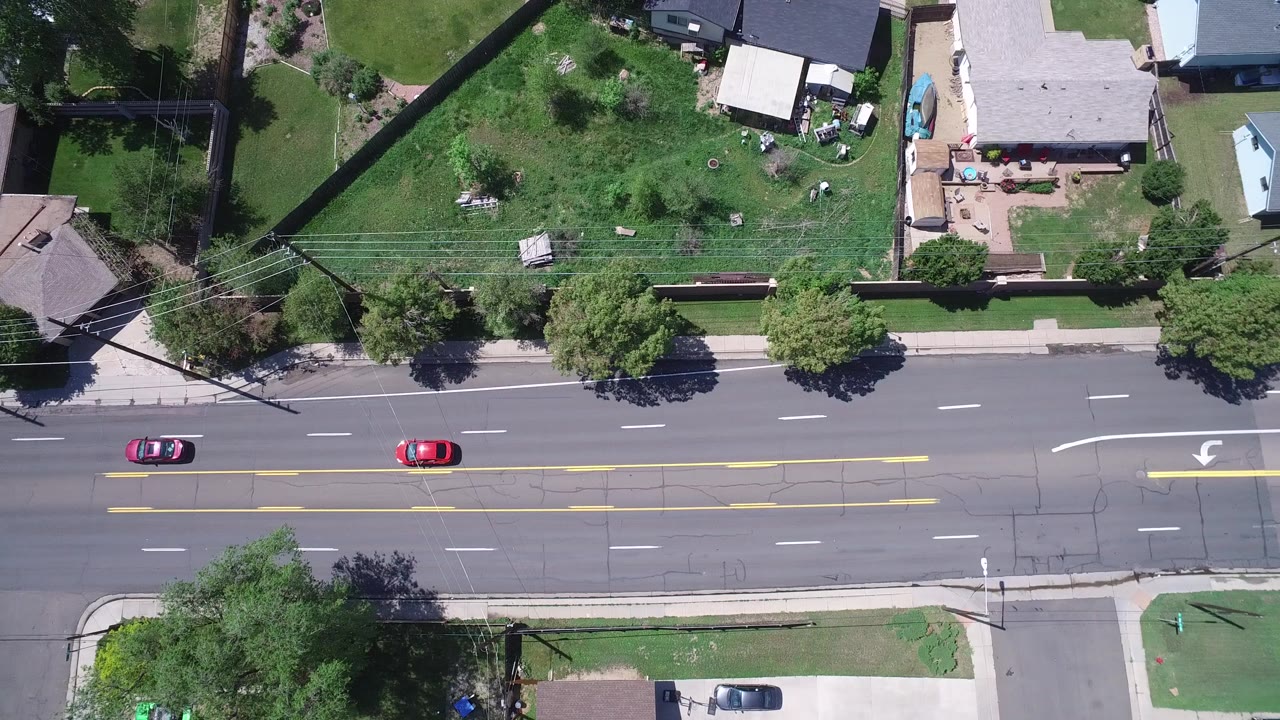 Overhead view of a wide avenue beside residential yards and homes.
