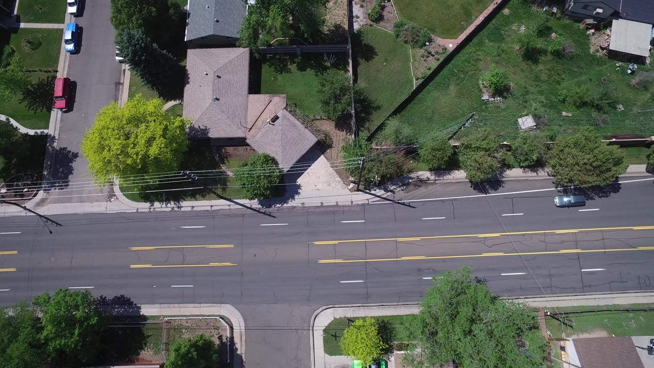 Overhead frame of a Westminster, Colorado residential road with houses, lawns, sidewalks, parked cars, trees, and no visible people.