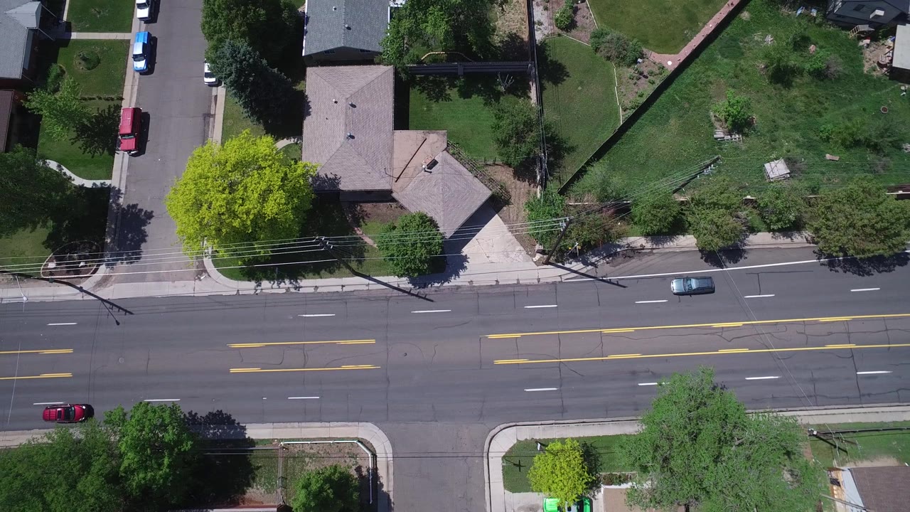 Top-down view of a wide road with homes and a red car