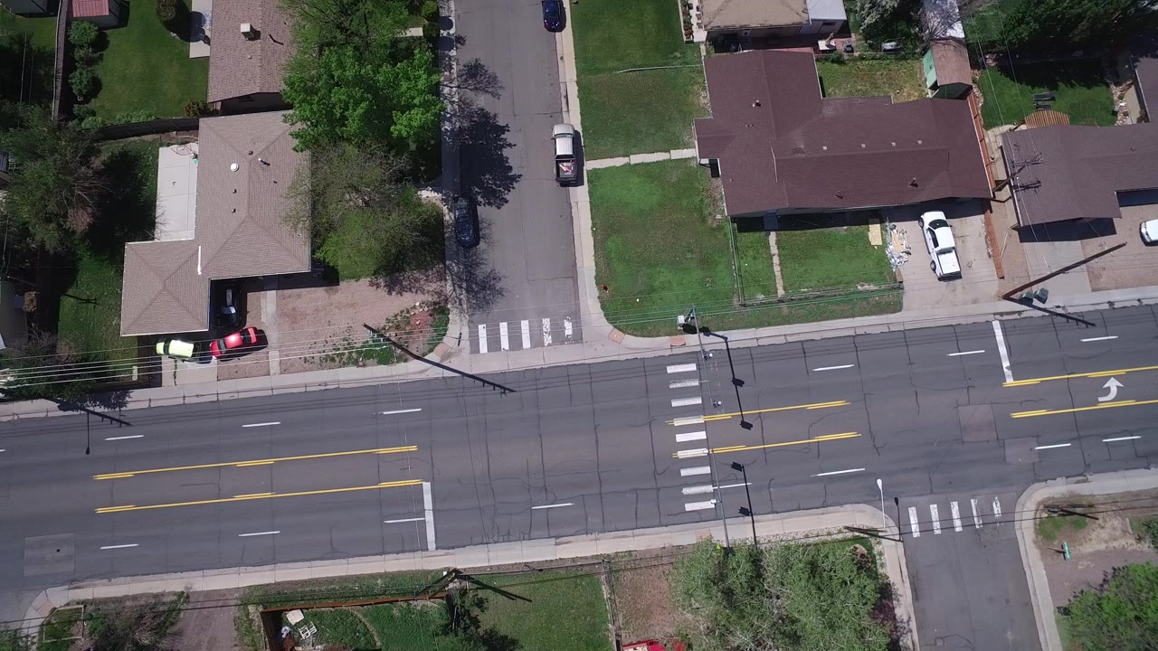 Overhead view in Westminster, Colorado of a multi-lane road crossing a residential side street, with crosswalks, lawns, private homes, parked cars, and no visible people.