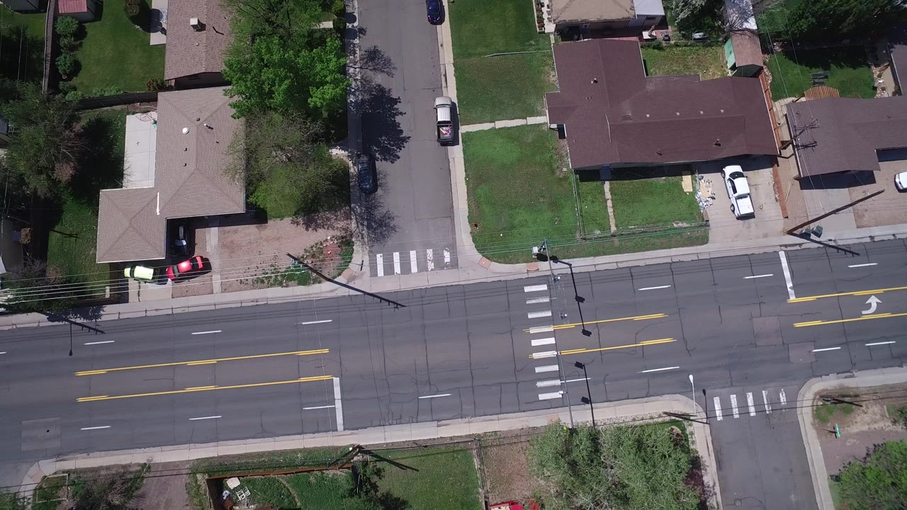 High-angle Westminster, Colorado frame with the main road running horizontally, a side street above it, green lawns, houses, parked vehicles, and no visible people.