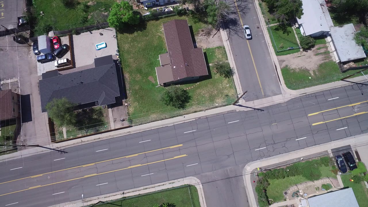 Overhead view of a suburban intersection with houses, lawns, sidewalks, and parked cars.