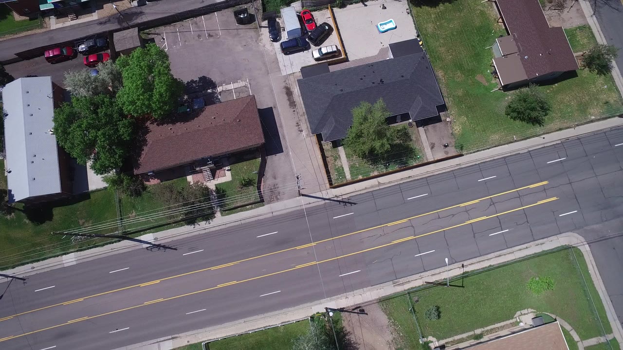 Overhead view of a multi-lane road beside buildings and parking lots.