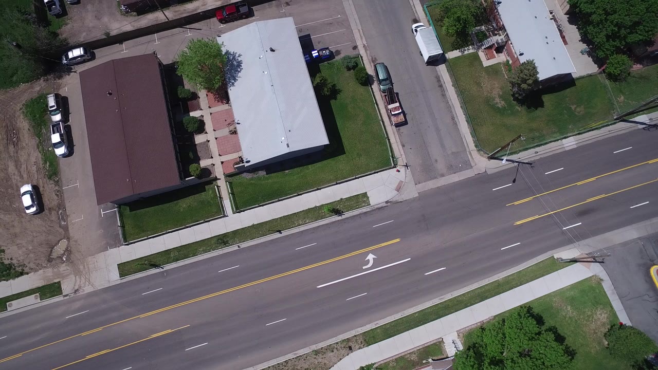 Overhead view of a main road beside low buildings and parked vehicles.