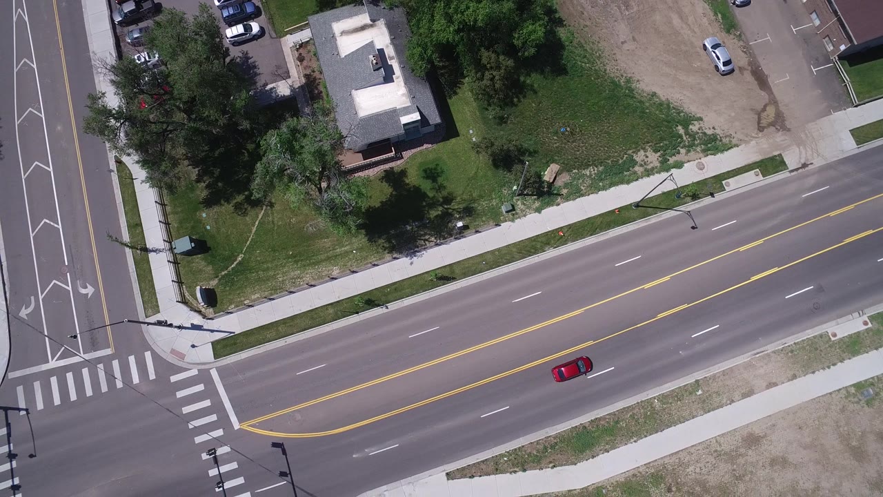 Top-down road scene with a red car on a quiet multi-lane street.