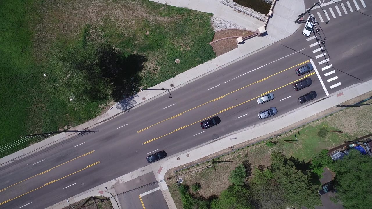 Overhead view of cars on a multi-lane road beside grass and sidewalks.