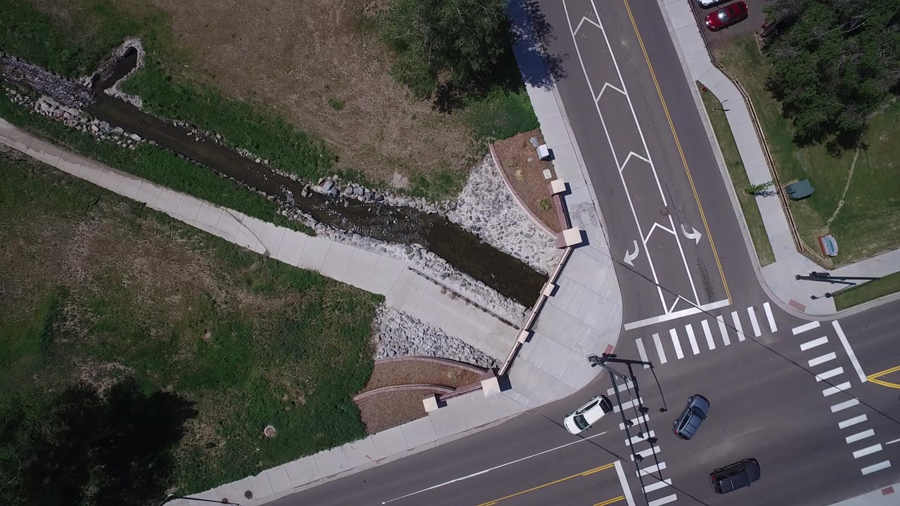 Overhead view of a road intersection beside grass and a narrow creek.
