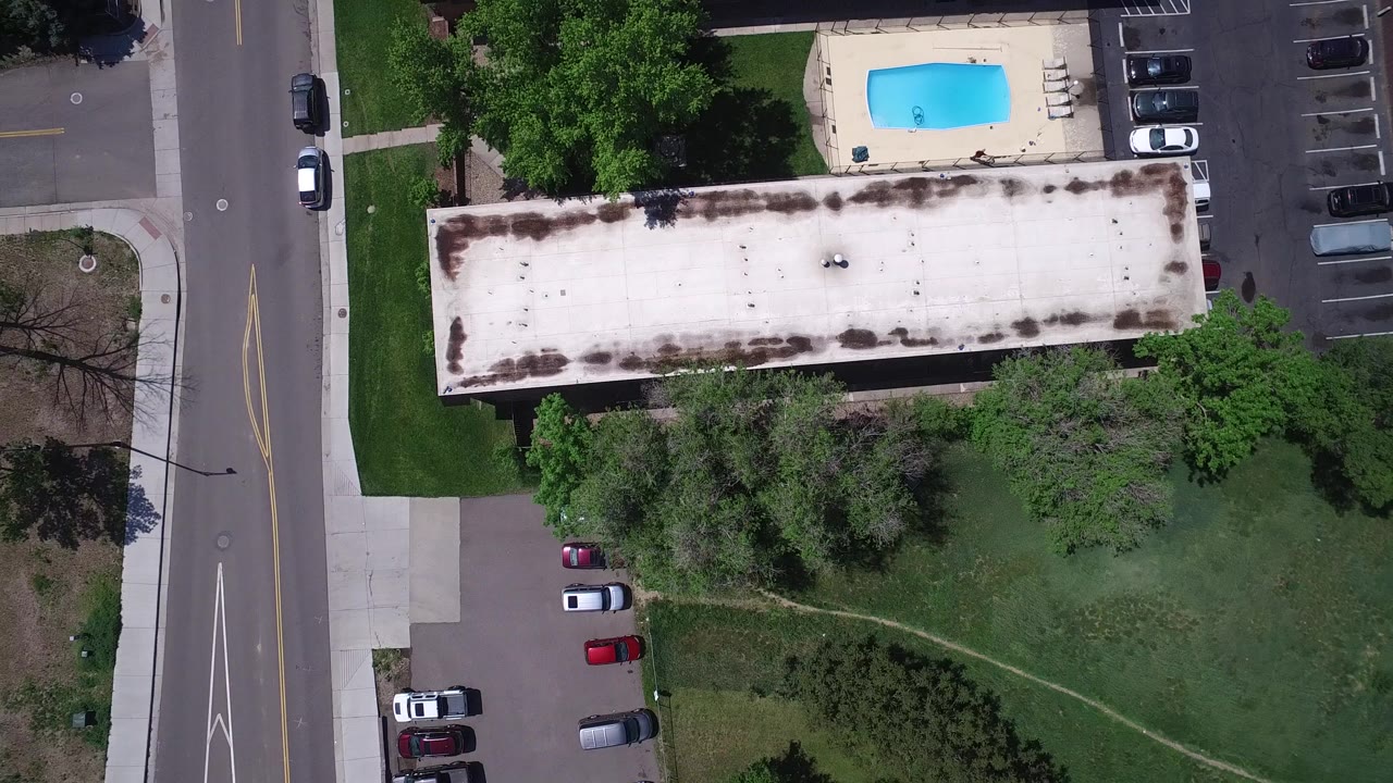 Overhead view of road, flat-roof building, trees, lawn, parking, and outdoor pool.