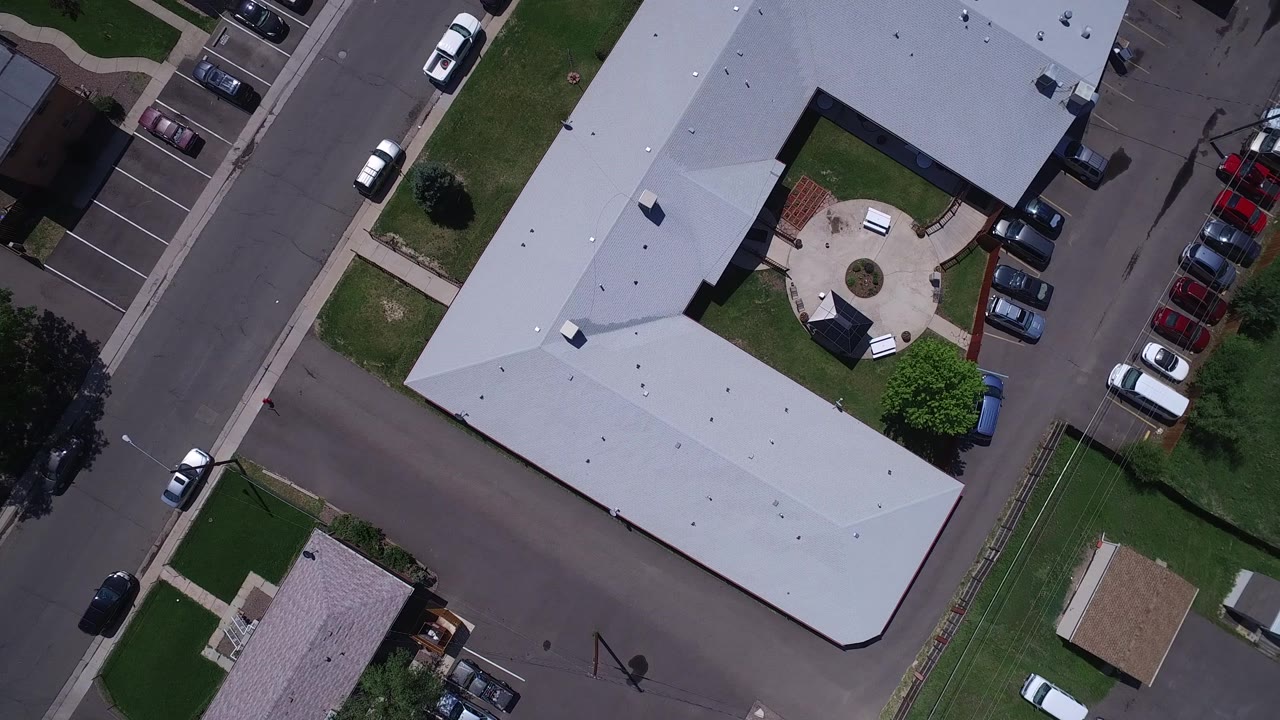 Aerial Westminster, Colorado view with the gray roof centered, a small paved courtyard visible inside the building shape, parked cars along the curb, and no visible people.