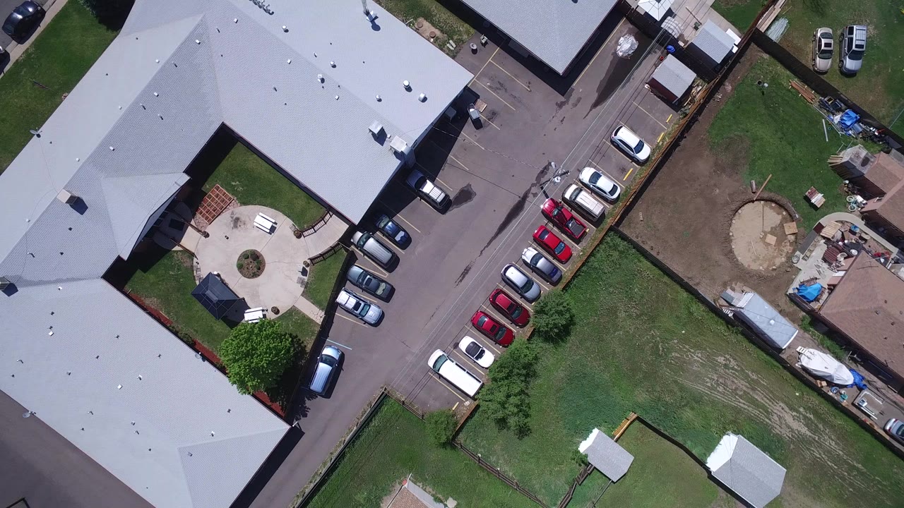 Overhead view of gray rooftops, parked cars, lawns, and fenced yards.