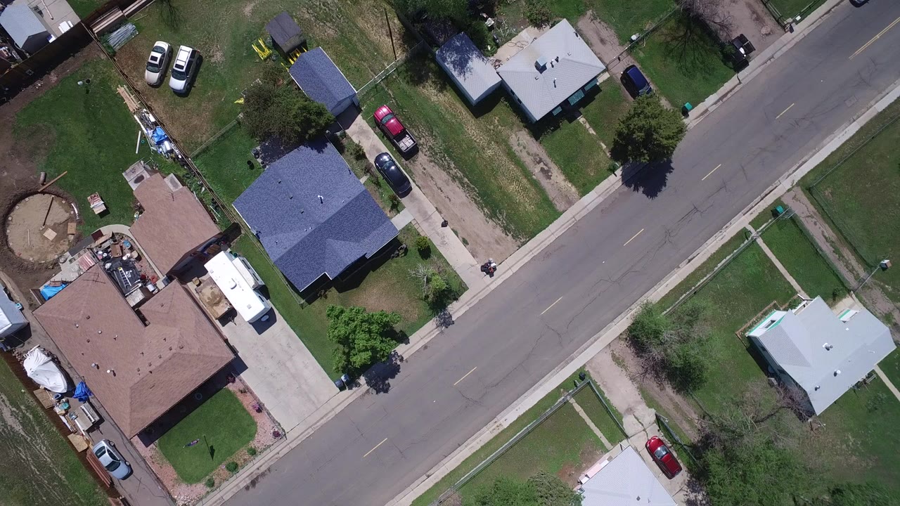 Top-down aerial view of homes, lawns, driveways, parked cars, and a residential street.