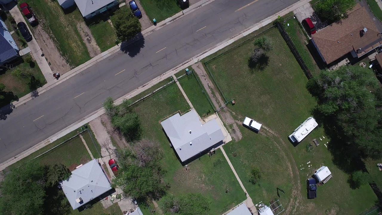 Overhead Westminster, Colorado view with a gray-roofed house near center, a white trailer or RV in a yard, parked cars, trees, sidewalks, and a residential road, with no visible people.