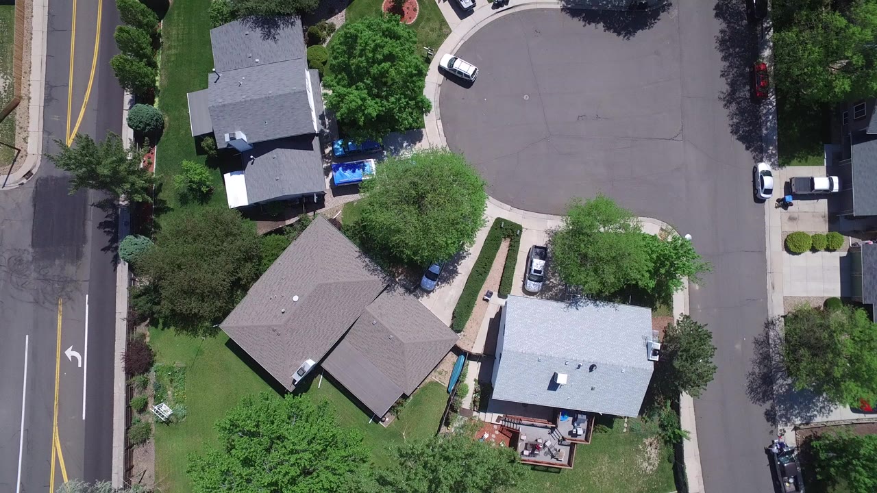 Top-down aerial view in Westminster, Colorado showing detached homes, lawns, trees, sidewalks, parked cars, and a curved residential street with no visible people.