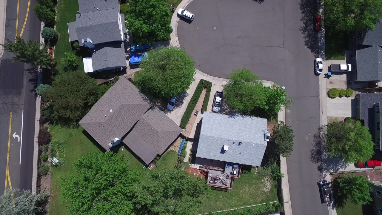 Drone view of houses, trees, and residential roads with cars parked along driveways.