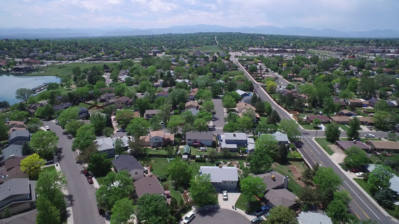 Aerial view of suburban homes, streets, trees, and a small lake.