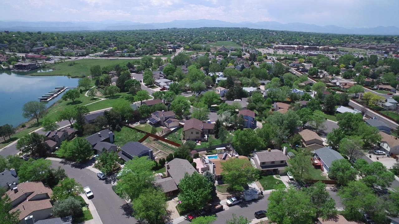 Aerial view of suburban homes, trees, streets, and a small lake.