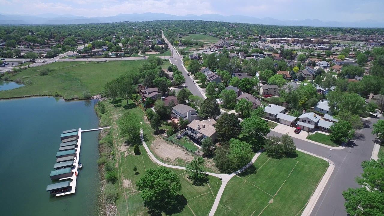 Aerial neighborhood view with lake docks, houses, open lawn, and a long road.