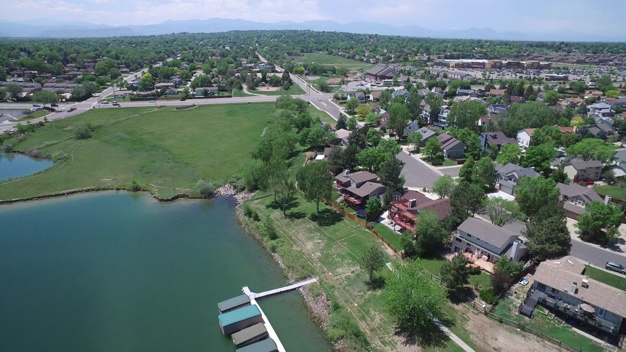 Aerial view over a lake, grassy shoreline, homes, roads, and distant mountains.