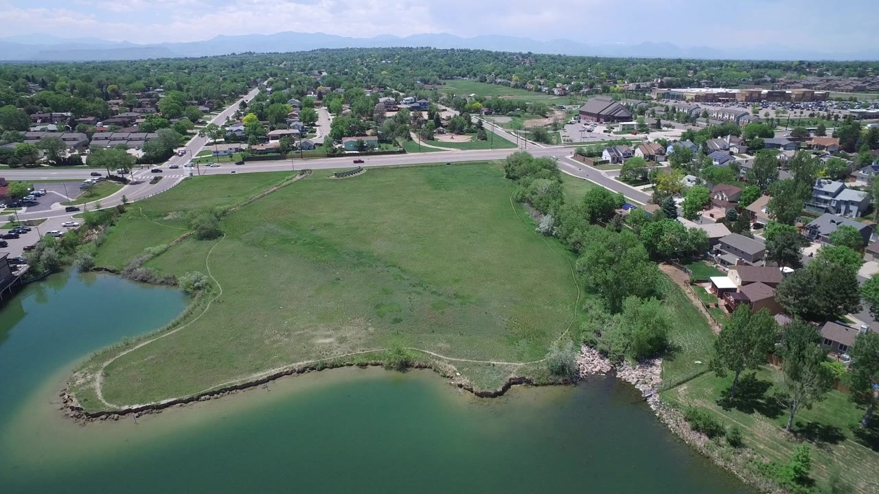 Aerial view of green lake water, open grass, roads, houses, and distant hills.