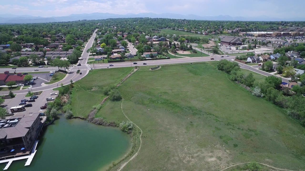 High view of a suburban road crossing above open grass and a small lake edge.