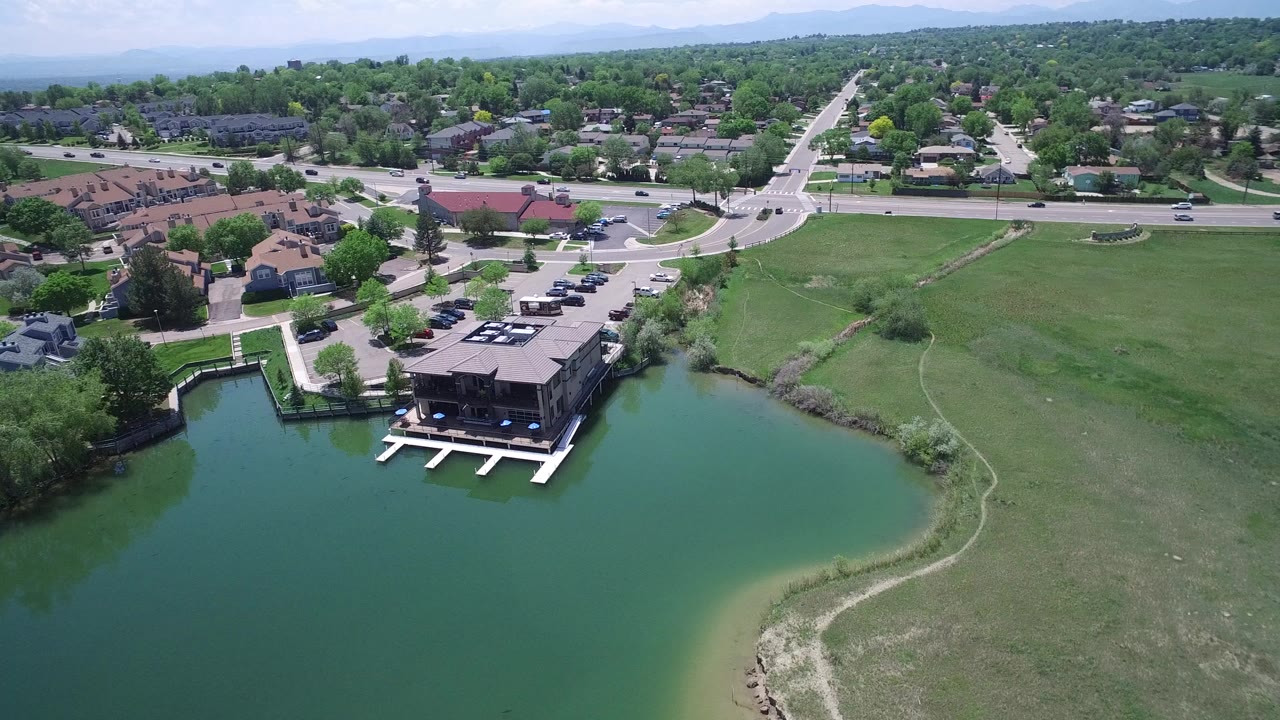 Aerial view of a green lake beside homes, docks, lawns, and a road.