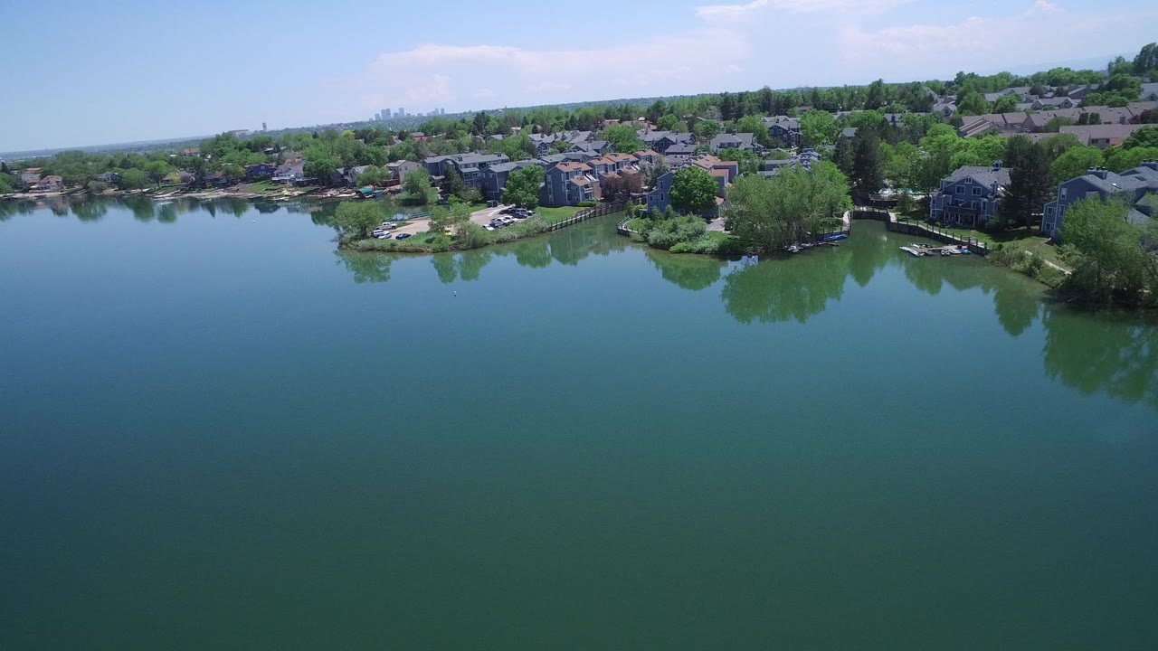 Aerial view over a lake toward waterfront homes and trees.